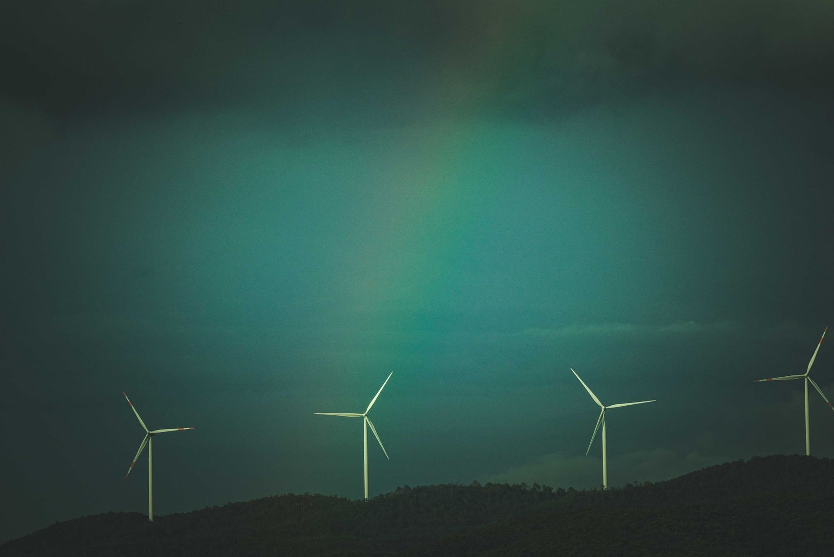 Wind turbines on a hillside under a dark green sky